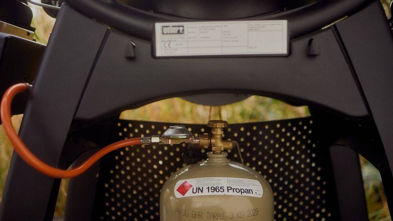 Eine Flasche Gas ist an einen Gasgrill angeschlossen.