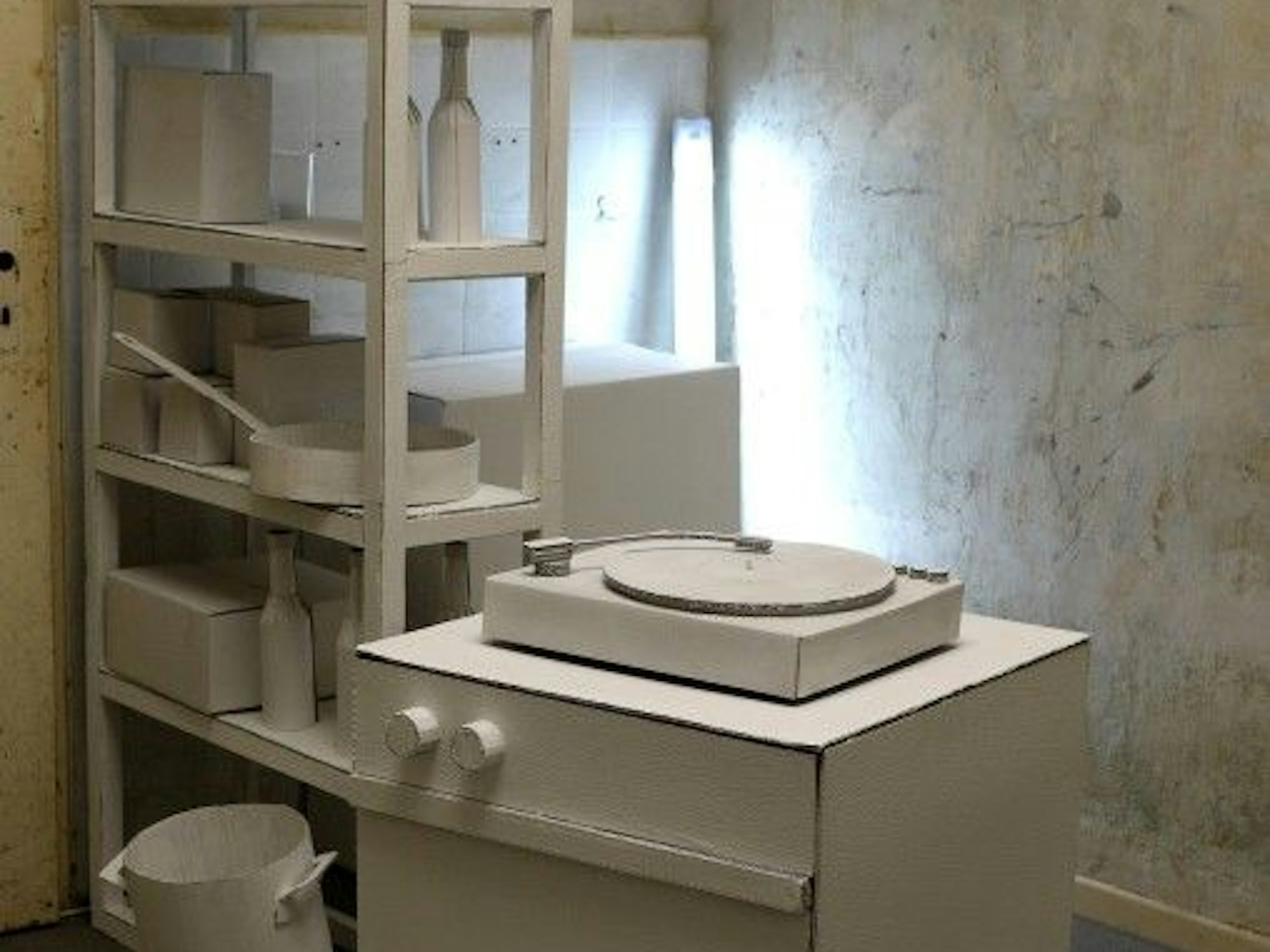 Weiße Papp-Küche mit Regal, Herd und Mülleimer, die nur von einer Lampe in der Ecke beleuchtet ist.