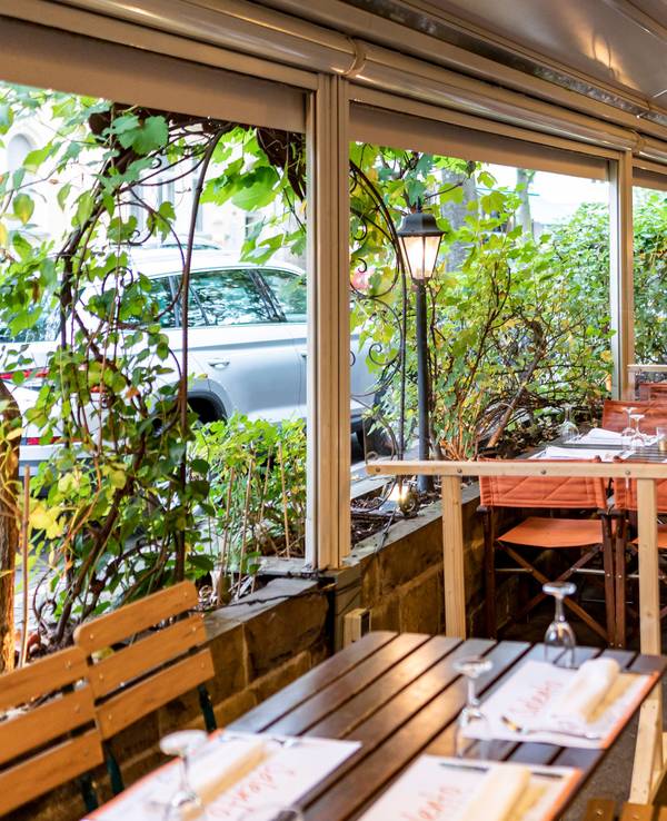 Kübel mit großen Pflanzen grenzen die Außengastronomie eines Restaurants vom Bürgersteig ab.