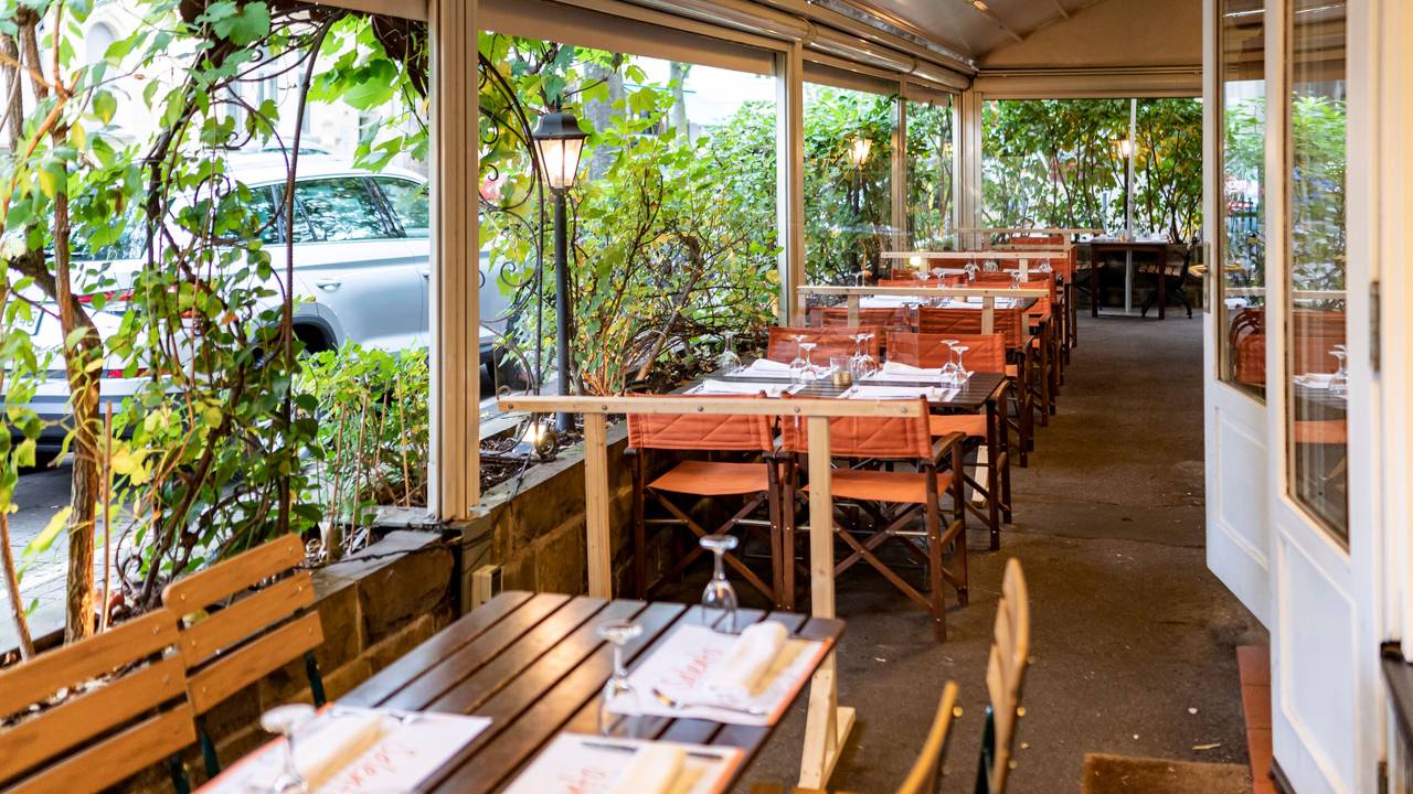 Kübel mit großen Pflanzen grenzen die Außengastronomie eines Restaurants vom Bürgersteig ab.