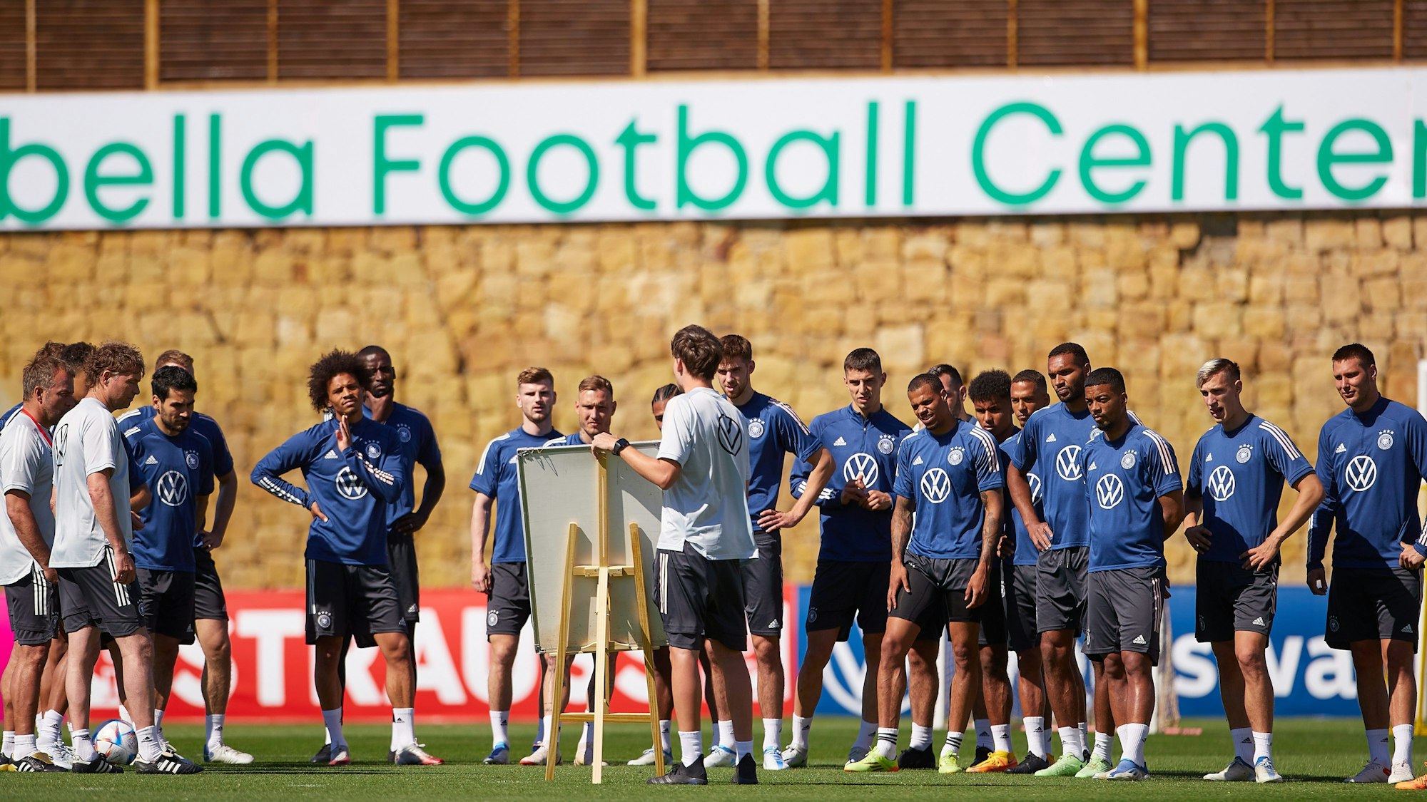 Die Nationalspieler stehen auf dem Platz und hören sich die Erklärungen an.