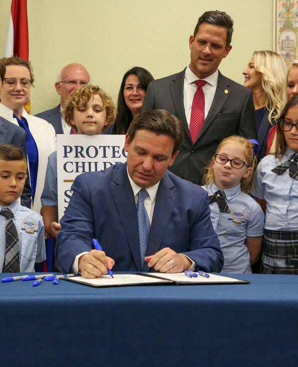 Gouverneur Ron DeSantis unterzeichnet ein Gesetz in Florida. Um ihn stehen mehrere Schülerinnen und Schüler.
