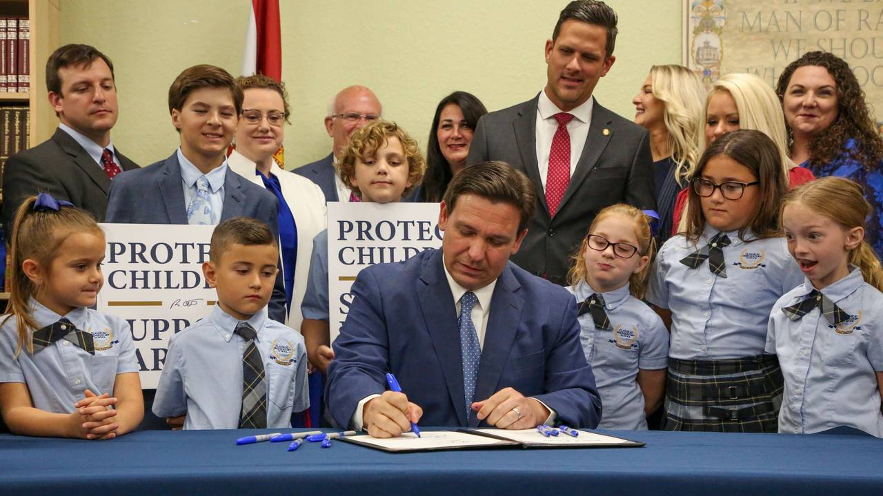 Gouverneur Ron DeSantis unterzeichnet ein Gesetz in Florida. Um ihn stehen mehrere Schülerinnen und Schüler.