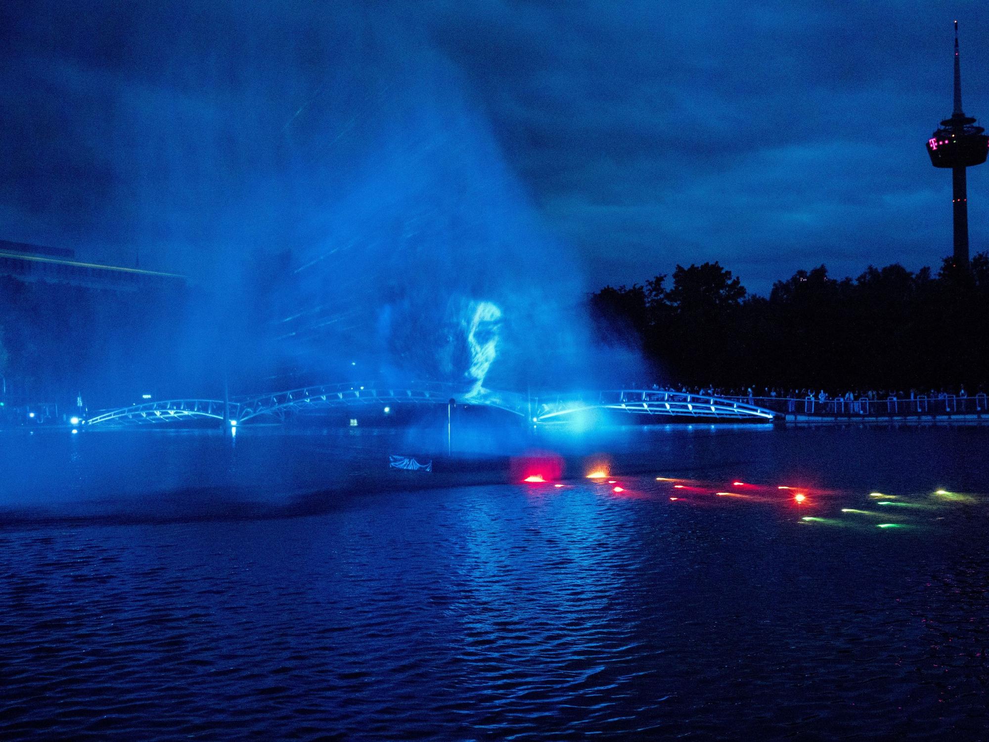 In der Lichtshow auf dem See im Kölner Mediapark wird das Gesicht einer Schauspielerin aus der Serie Stranger Things auf Wassernebel projiziert.