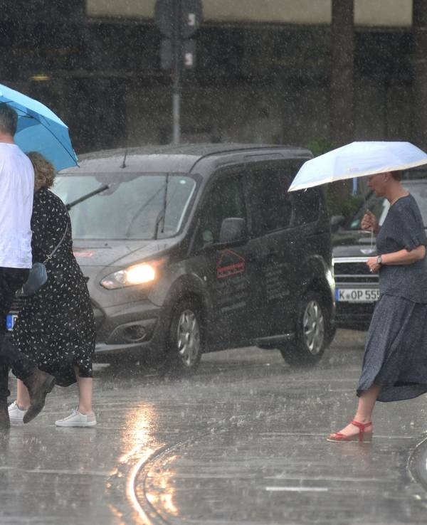 Menschen laufen in Köln mit Regenschirmen über die nassen Straßen.