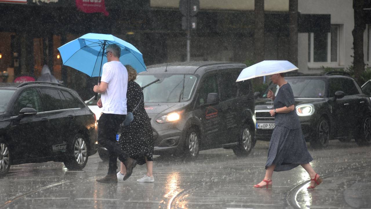 Menschen laufen in Köln mit Regenschirmen über die nassen Straßen.
