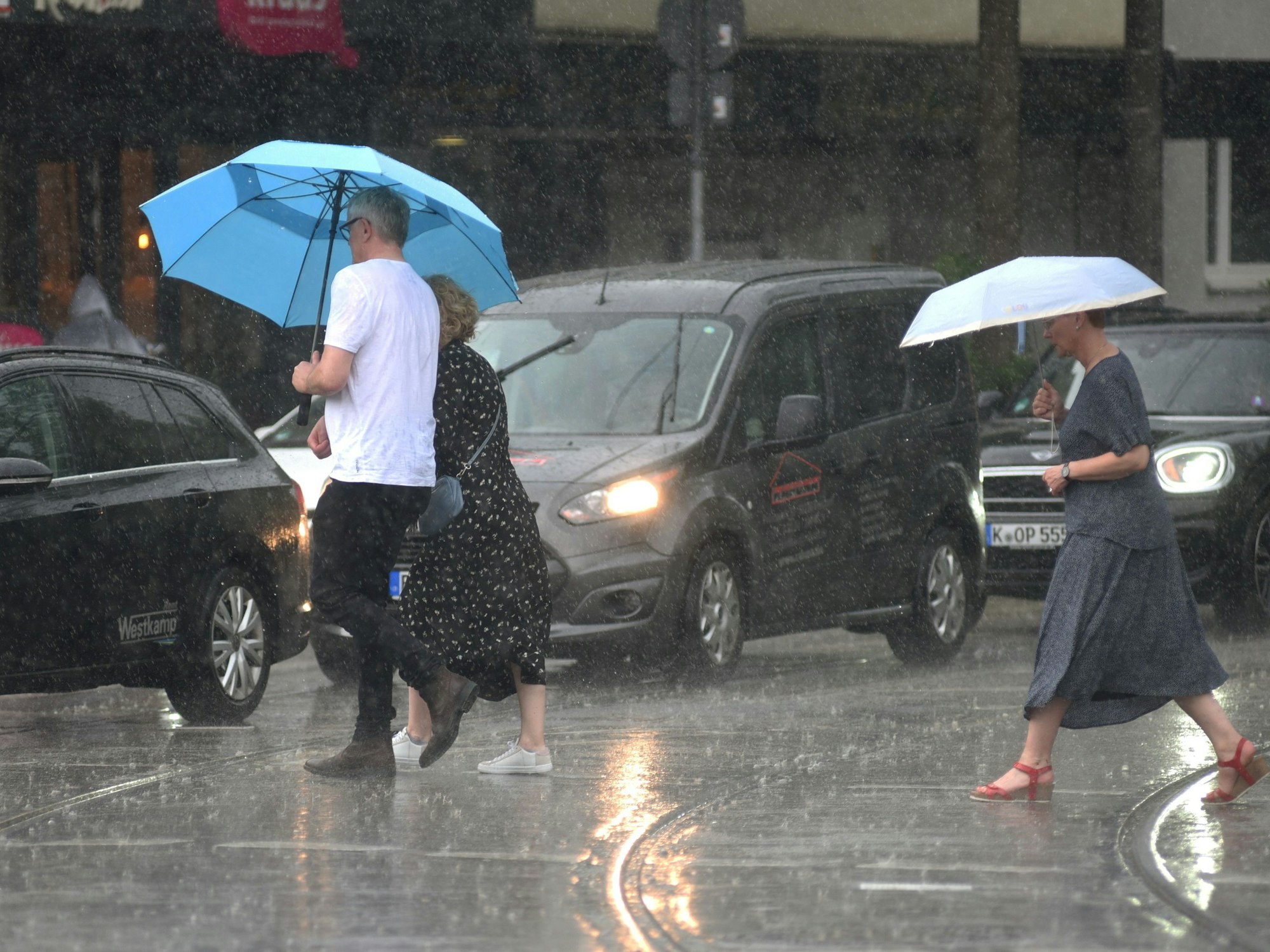Menschen laufen in Köln mit Regenschirmen über die nassen Straßen.