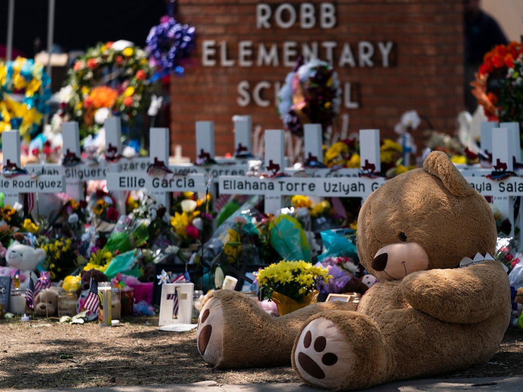 Ein großer Teddy-Bär und viele Blumen liegen vor der Gedenkstätte der Grundschule in Uvalde, Texas.