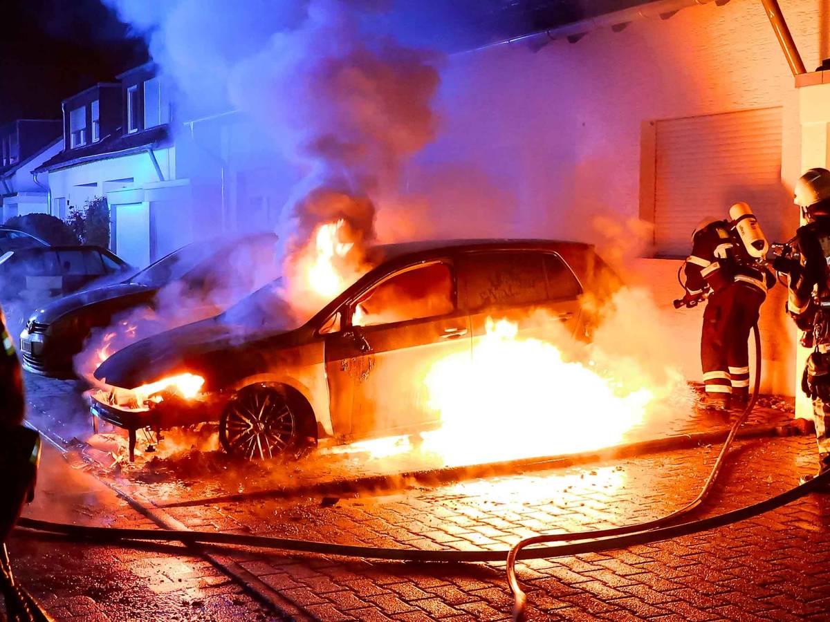 Feuer in Köln: Ein Auto steht in Flammen, mehrere Feuerwehrmänner sind im Einsatz.