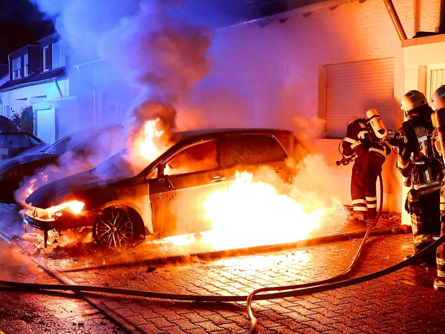 Ein Auto brennt lichterloh vor einem Haus, mehrere Feuerwehrmänner sind im Einsatz.