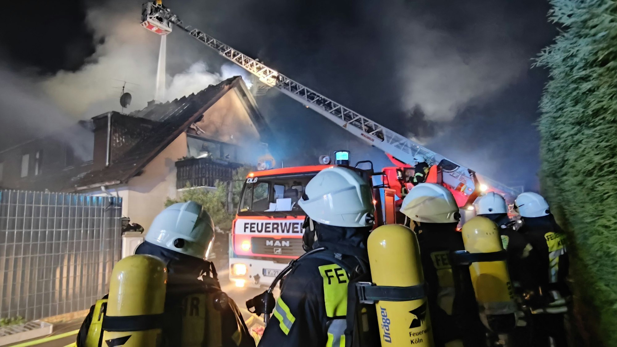 Feuerwehrleute stehen vor einem brennenden Haus.