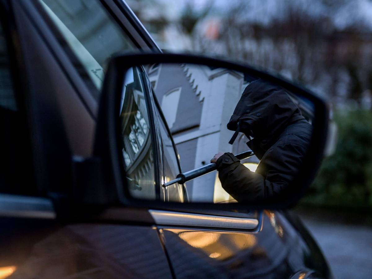 Ein Mann versucht eine Autotür mit einer Metallstange aufzubrechen.