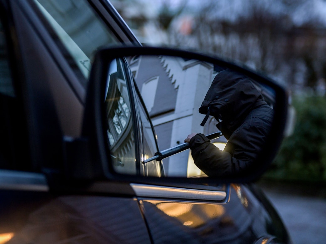 Ein Mann versucht eine Autotür mit einer Metallstange aufzubrechen.