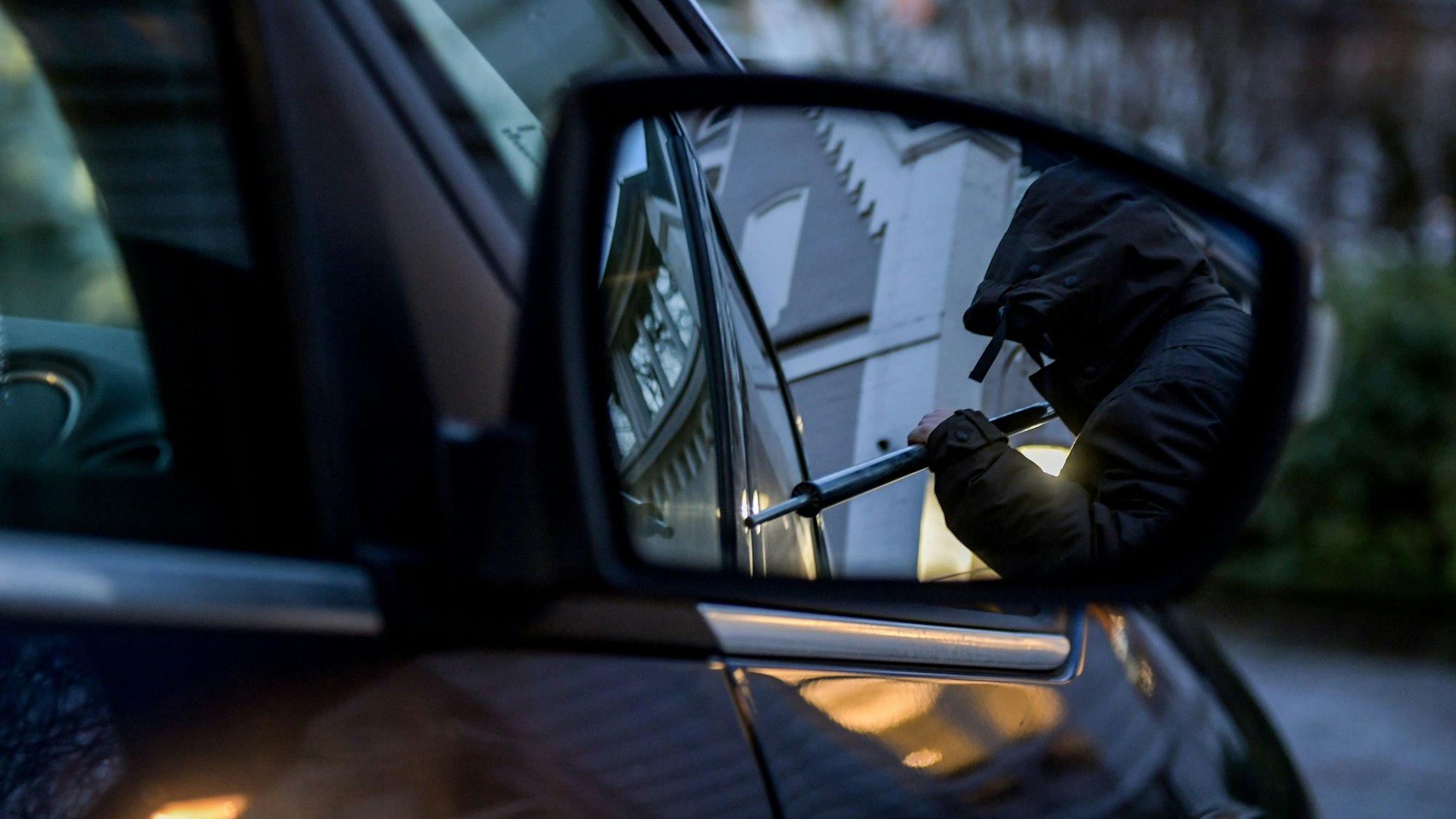 Ein Mann versucht eine Autotür mit einer Metallstange aufzubrechen.