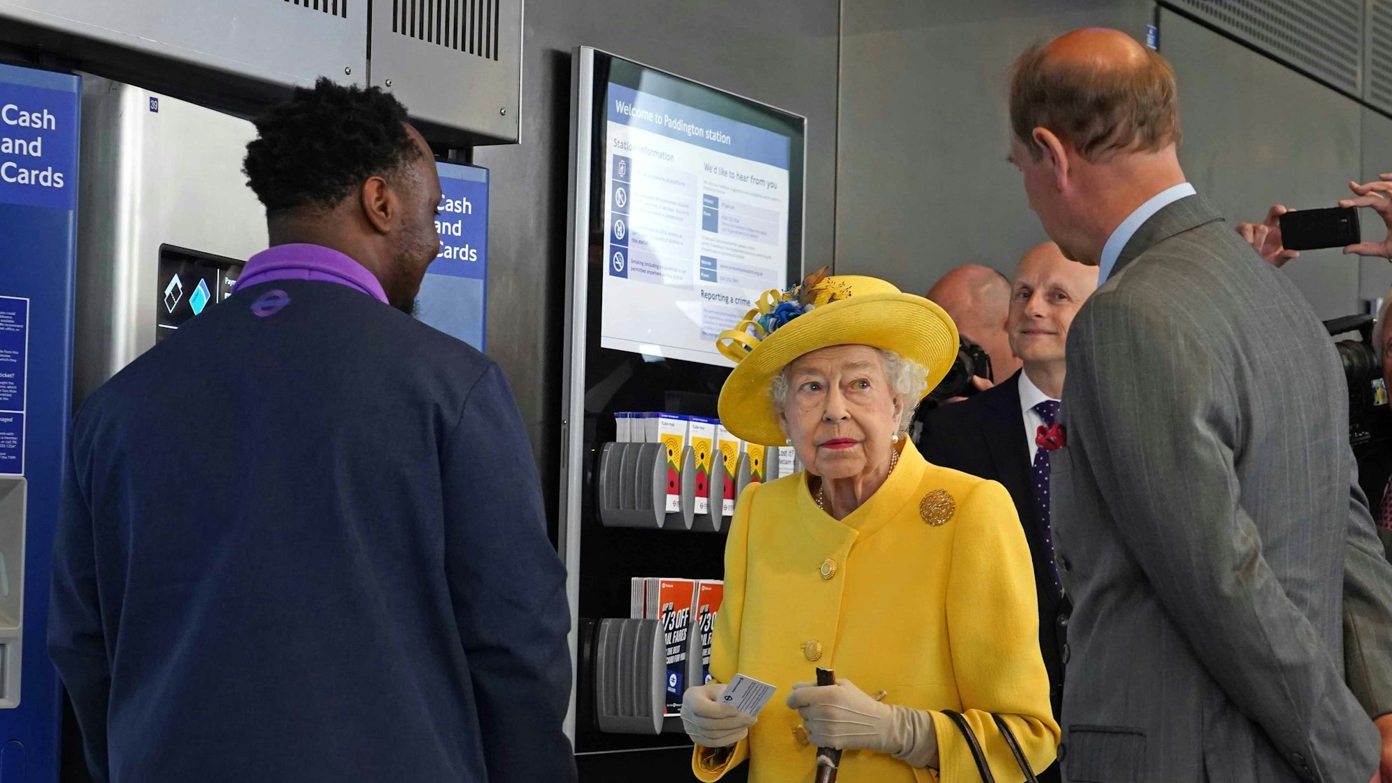 Die britische Königin Elizabeth II. (M) und Prinz Edward (r), Earl of Wessex, stehen während ihres Besuchs des Bahnhofs Paddington anlässlich der Fertigstellung des Londoner Bahnprojekts "Crossrail" neben einem Fahrkartenautomaten.