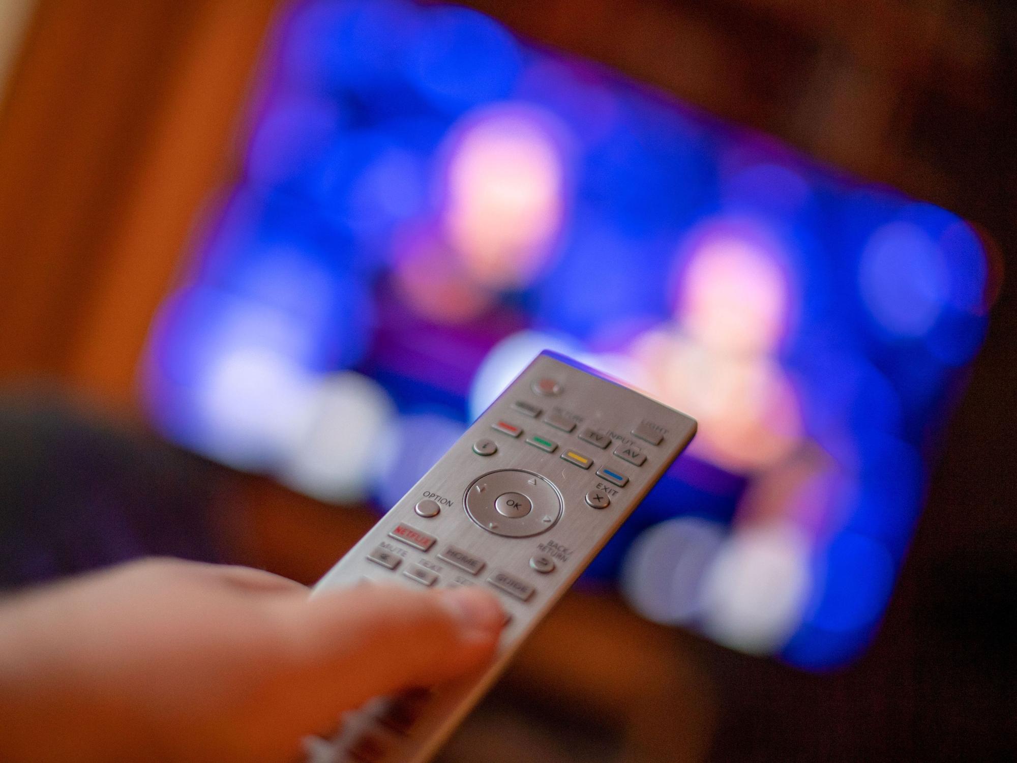 Ein Mann bedient mit der Fernbedienung einen Fernseher (gestellte Szene).