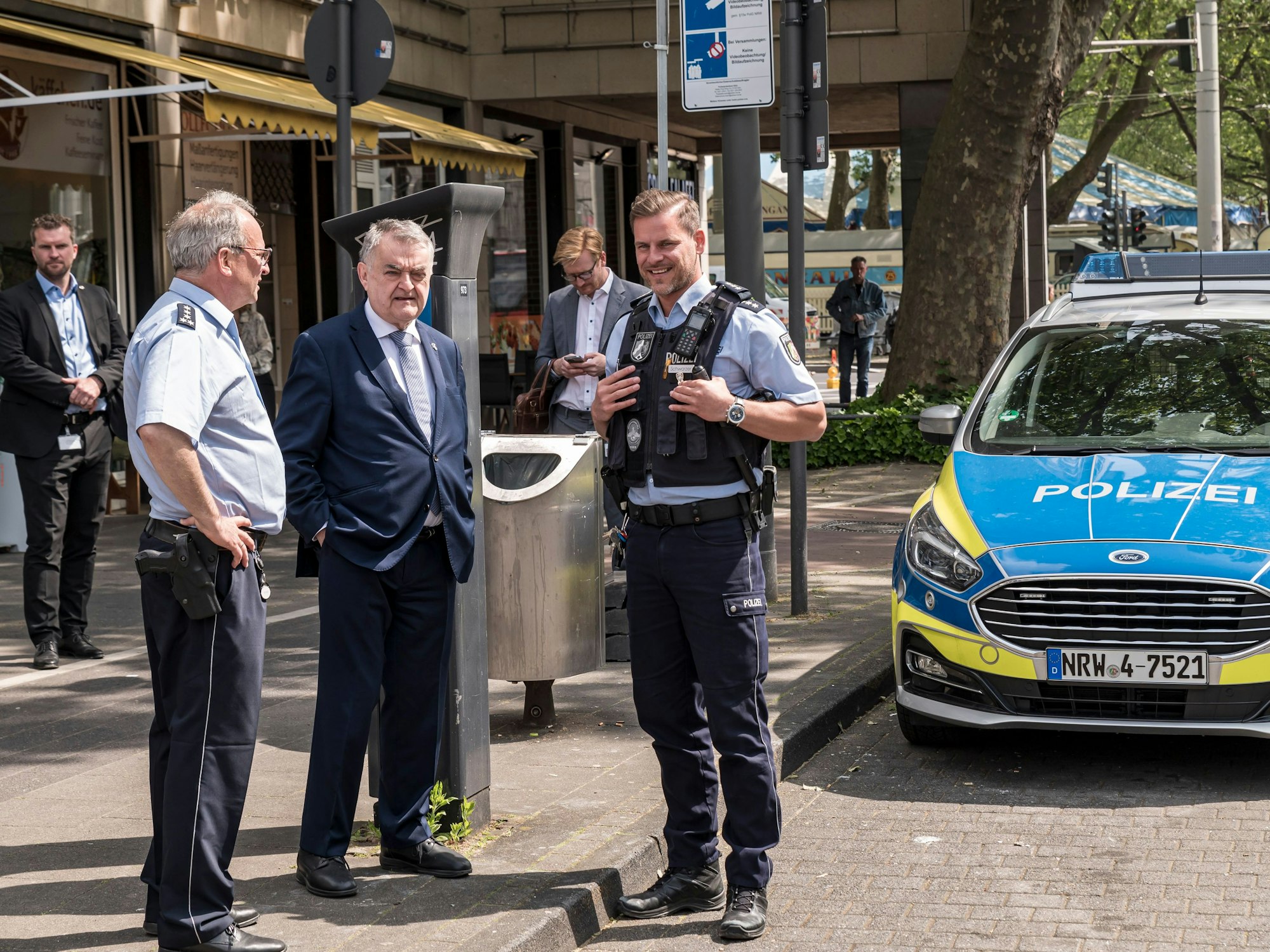 Innenminister Herbert Reul im Gespräch mit zwei Polizisten vor einem Streifenwagen am Neumarkt.