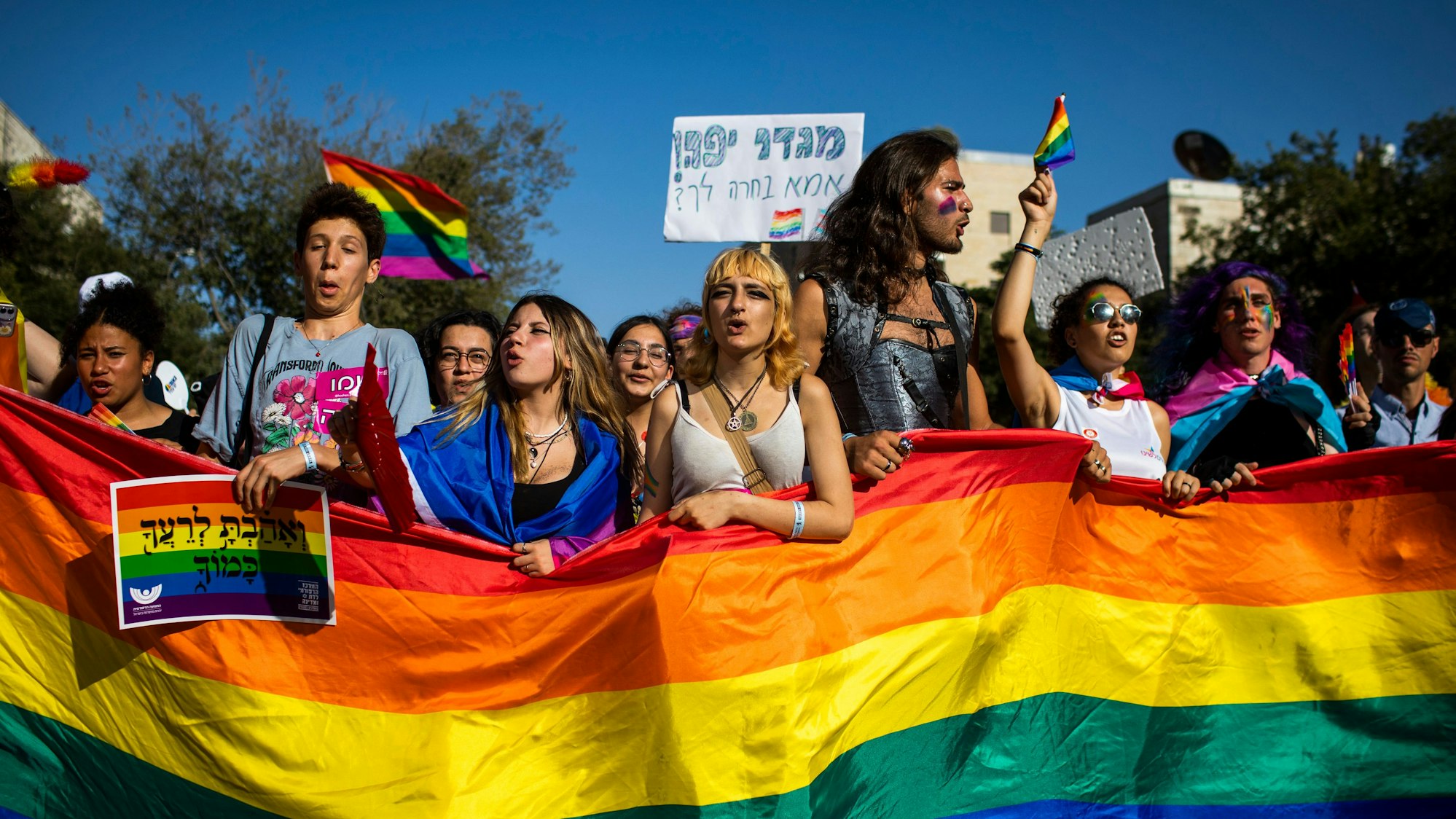 Menschen marschieren mit Regenbogenfahnen und Schildern während der jährlichen Gay-Pride-Parade durch die Straßen.