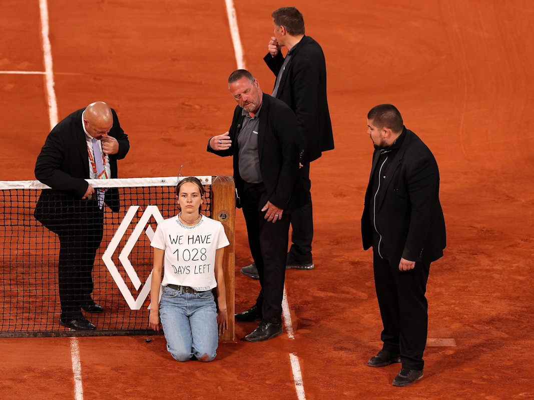 Sicherheitsmitarbeiter stehen um die Aktivistin am Netz bei den French Open.