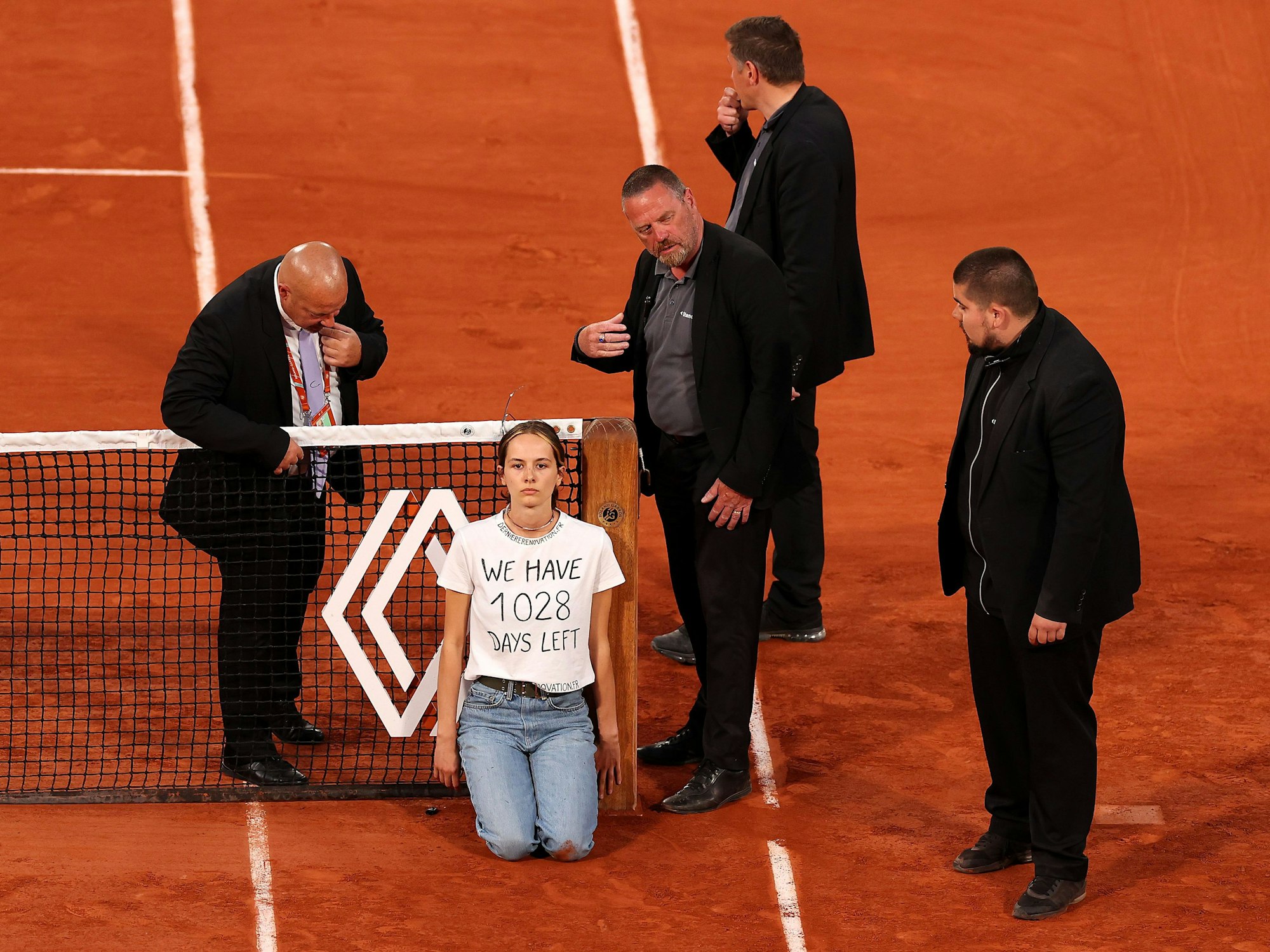 Sicherheitsmitarbeiter stehen um die Aktivistin am Netz bei den French Open.