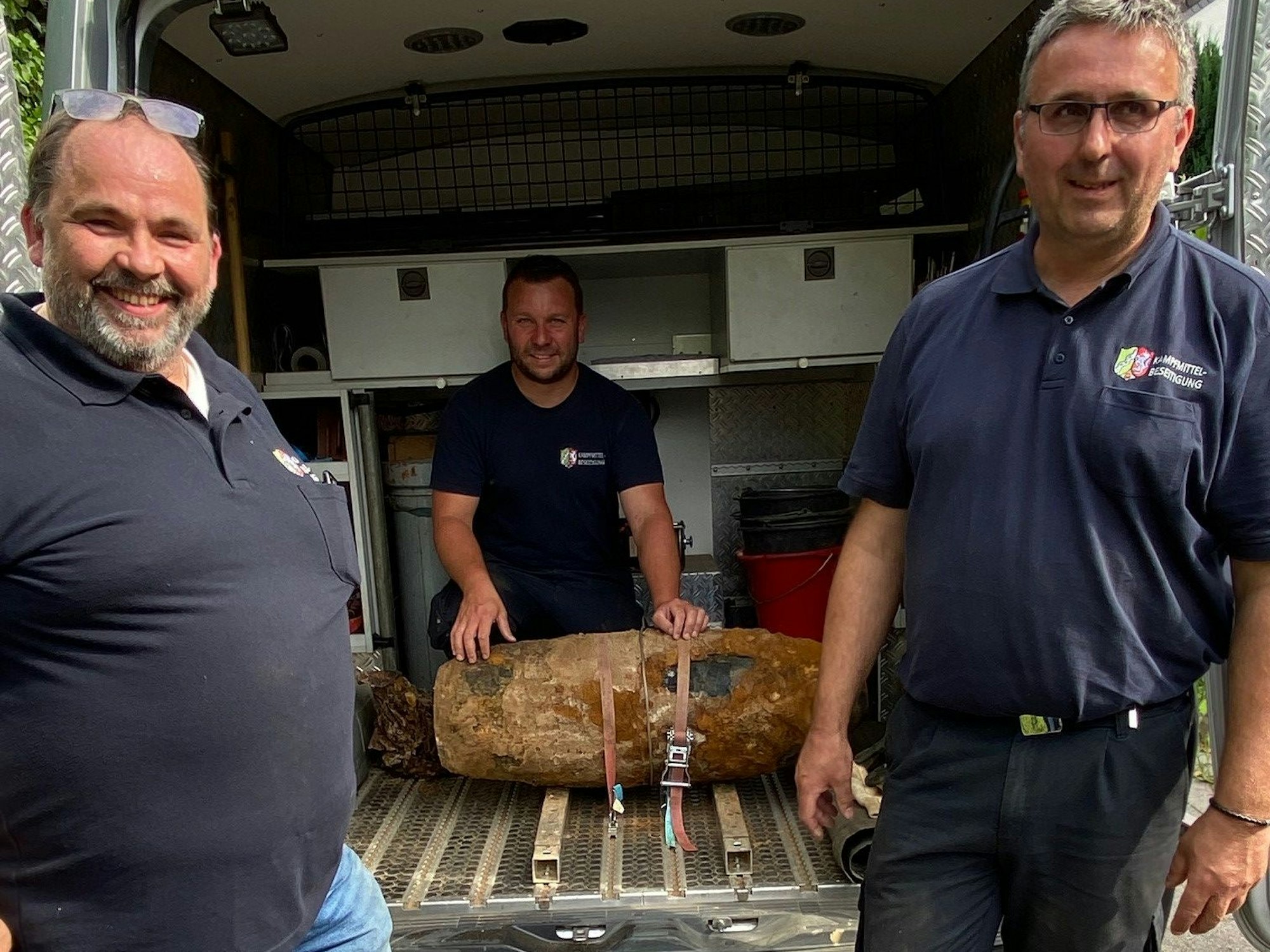 Drei Männer stehen vor einer entschärften Bombe.