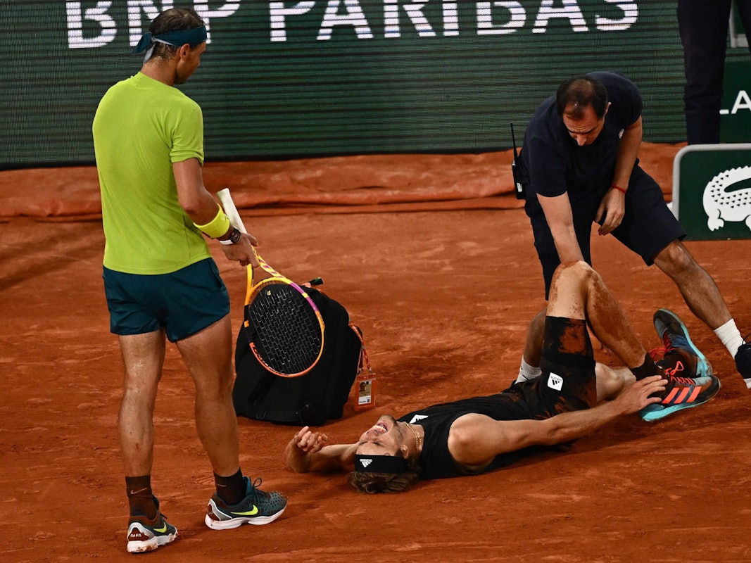 Alexander Zverev liegt schreiend am Boden, während ihn ein Arzt behandelt. Gegenspieler Rafael Nadal leidet daneben mit.