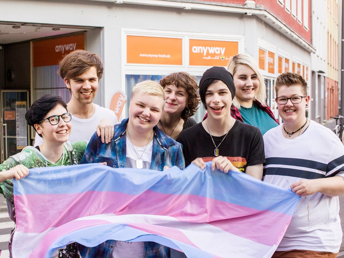 Jugendliche stehen mit Regenbogen-Fahne auf einer Straße in Köln.