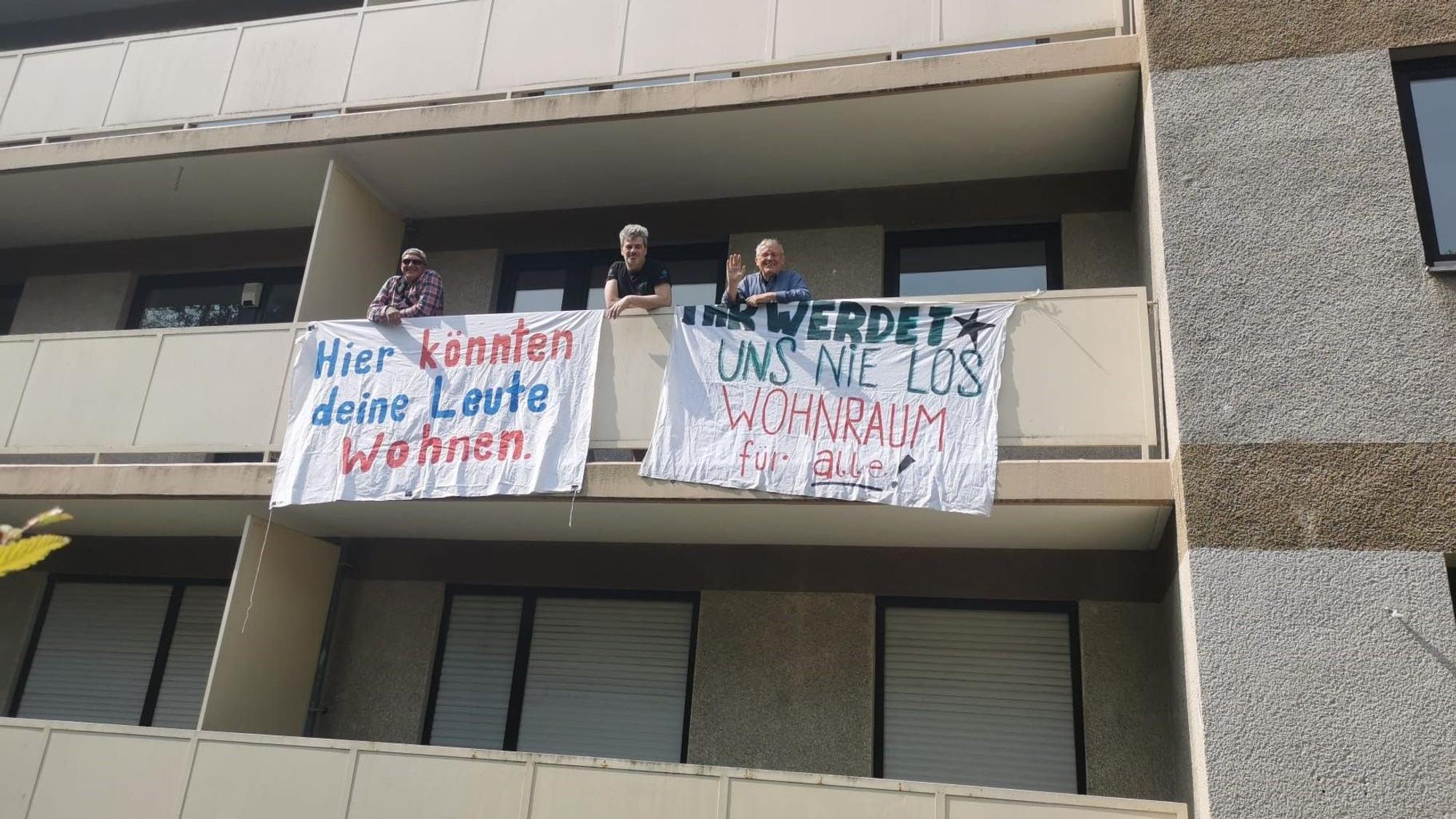 Aktivisten stehen auf einem Balkon und haben Plakate aufgehängt, unter anderem mit der Aufschrift: „Hier könnten deine Leute wohnen“.