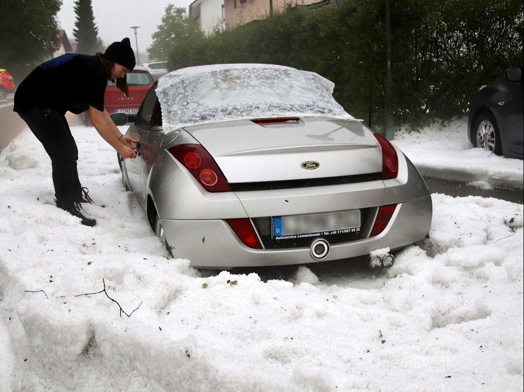 Eine Frau versucht am Sonntag, 5. Juni 2022, ein Auto aufzuschließen, das am Rand einer von Hagelkörnern bedeckten Straße steht.