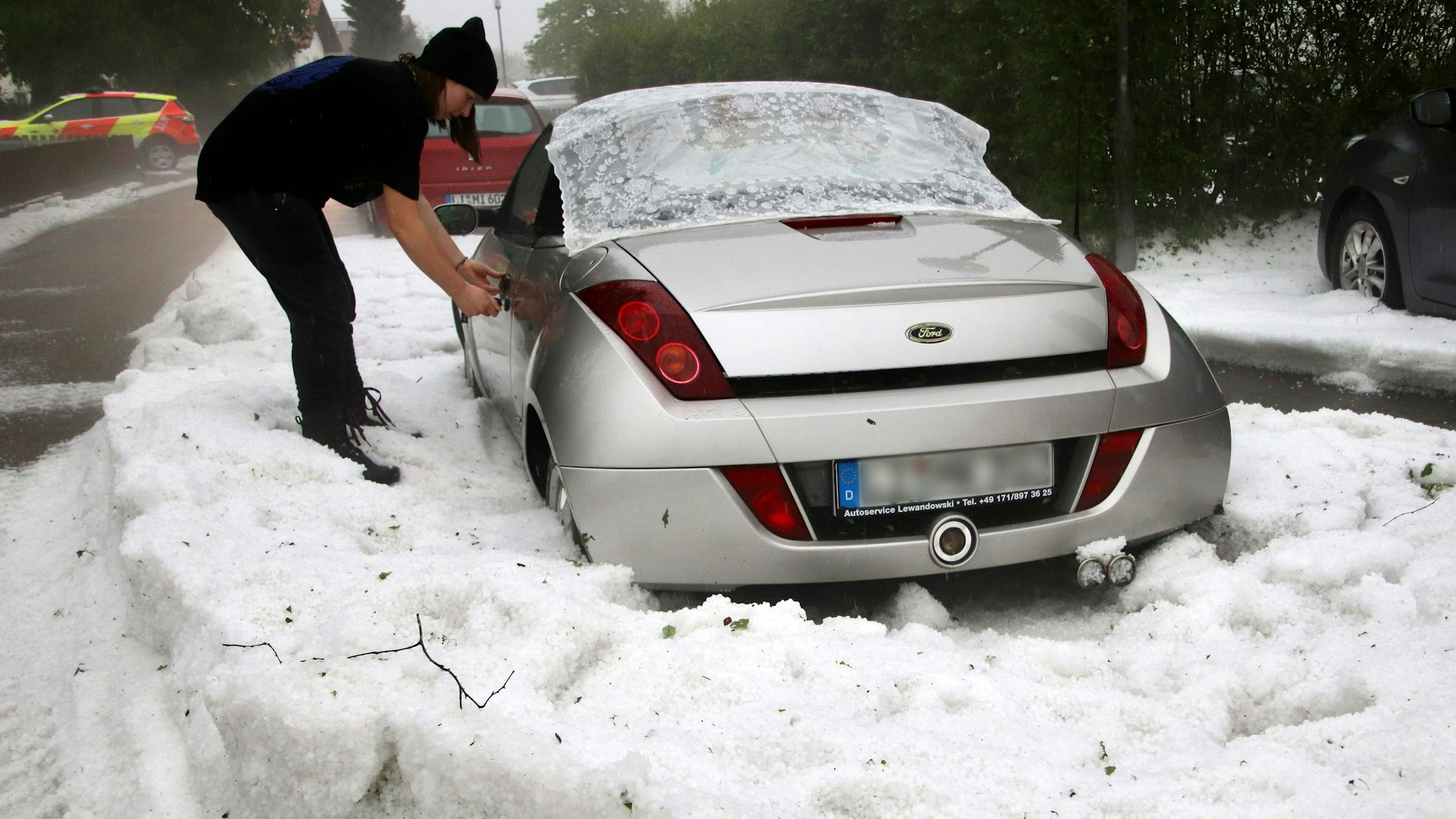 Eine Frau versucht am Sonntag, 5. Juni 2022, ein Auto aufzuschließen, das am Rand einer von Hagelkörnern bedeckten Straße steht.