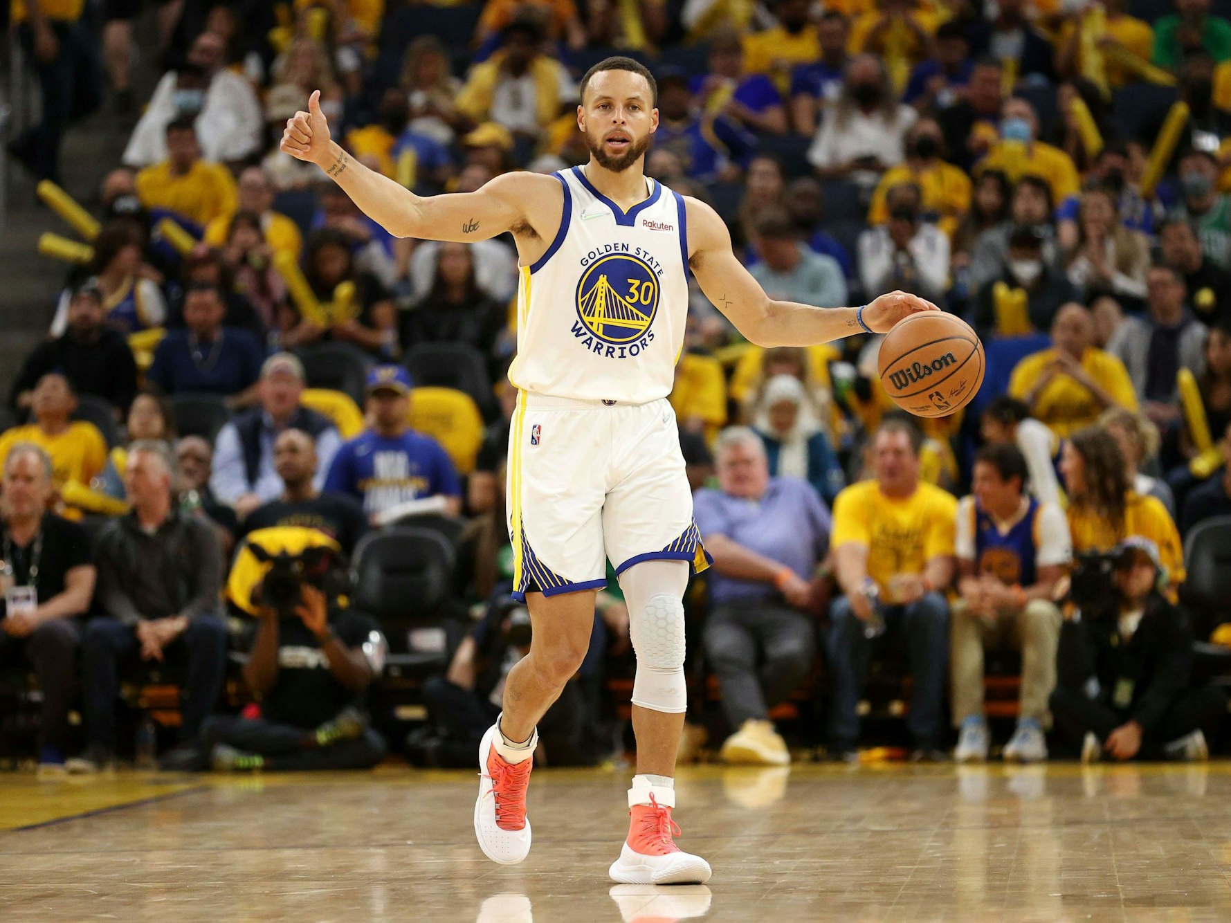Steph Curry dribbelt mit der einen Hand, während er mit der anderen einen Daumen nach oben zeigt.