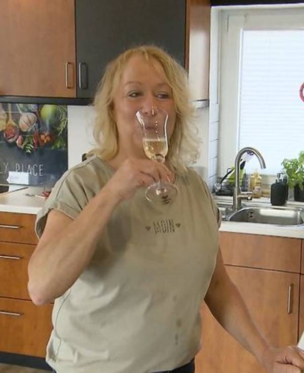 Friseurmeisterin Hiltrud steht bei „Das perfekte Dinner“ mit einem Glas Sekt in der Küche.