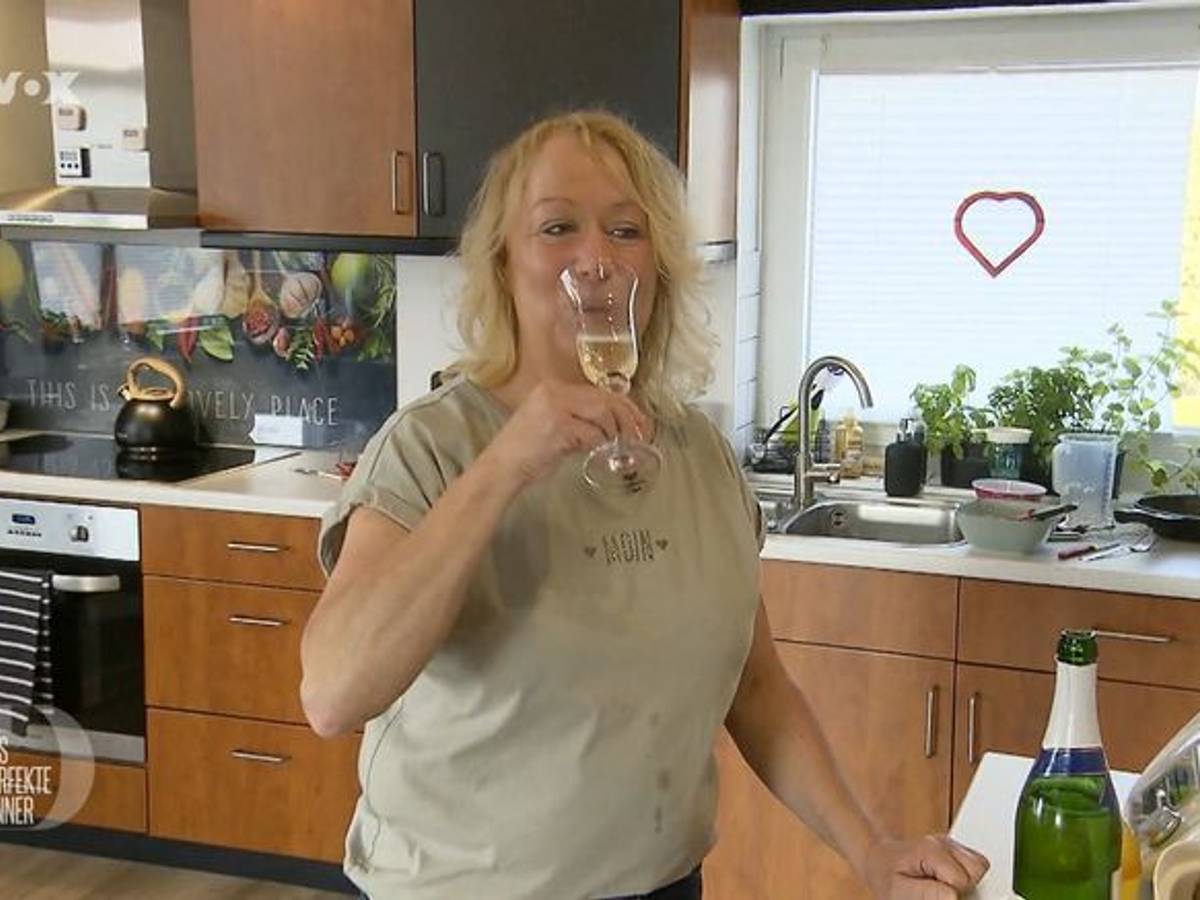 Friseurmeisterin Hiltrud steht bei „Das perfekte Dinner“ mit einem Glas Sekt in der Küche.