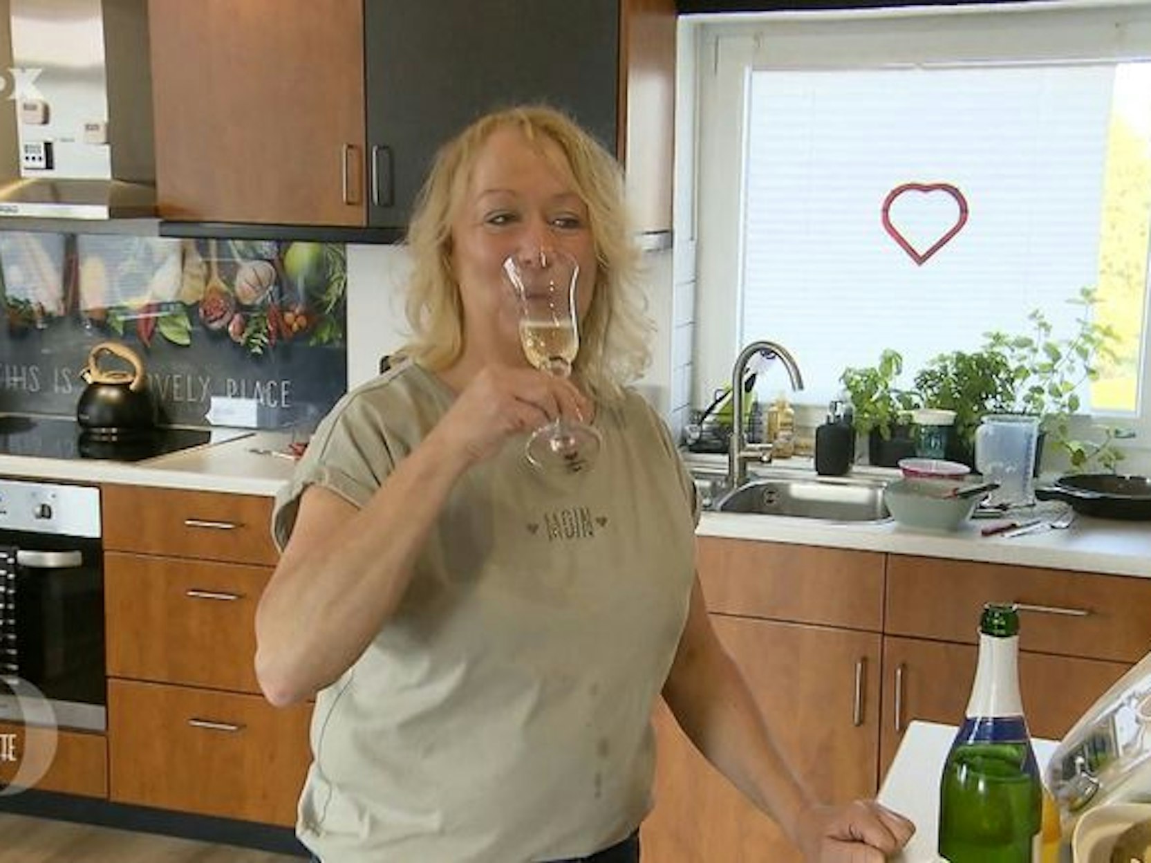 Friseurmeisterin Hiltrud steht bei „Das perfekte Dinner“ mit einem Glas Sekt in der Küche.