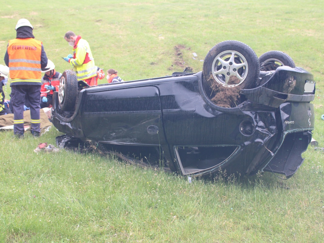 Einsatzkräfte kümmern sich um den Fahrer, der vor seinem Auto liegt.