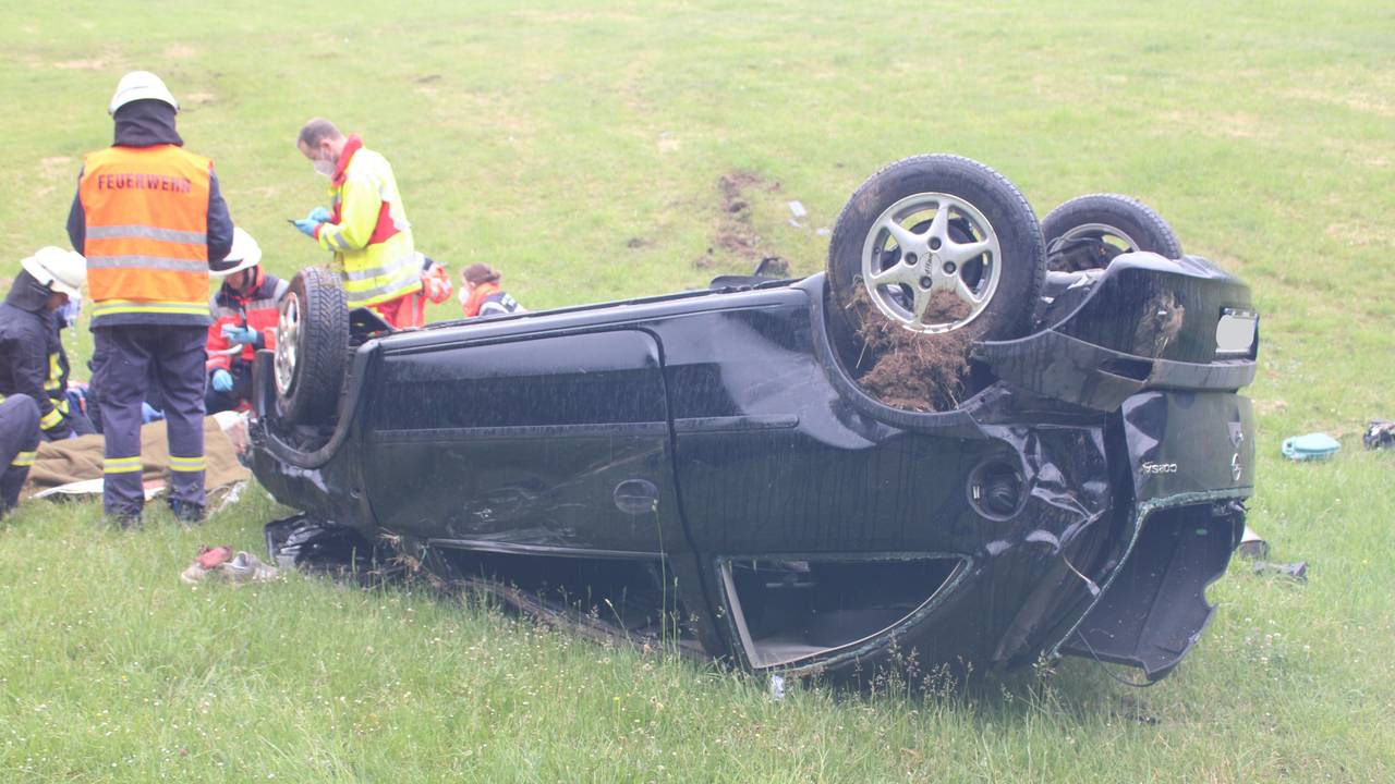 Einsatzkräfte kümmern sich um den Fahrer, der vor seinem Auto liegt.