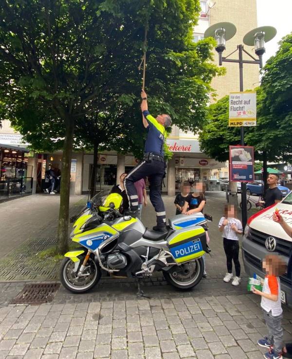 Ein Motorradpolizist aus Hagen steht auf seinem Motorrad, um einen Ball aus einem Baum zu holen.