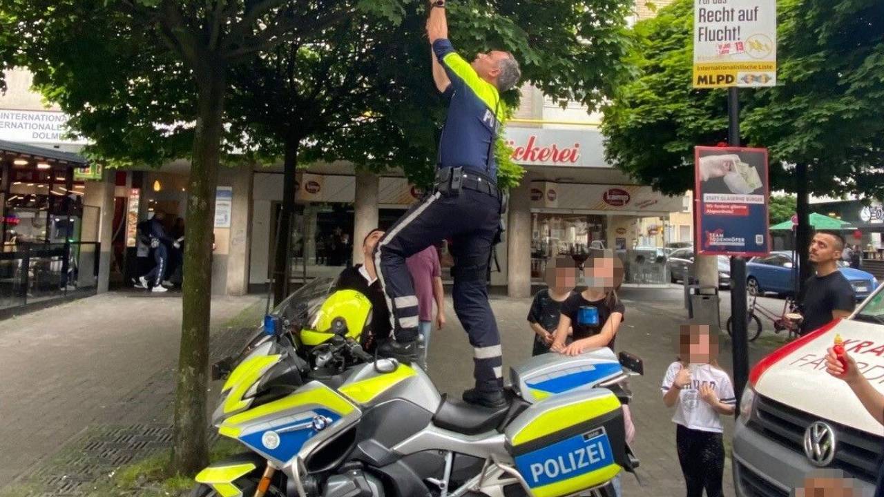 Ein Motorradpolizist aus Hagen steht auf seinem Motorrad, um einen Ball aus einem Baum zu holen.