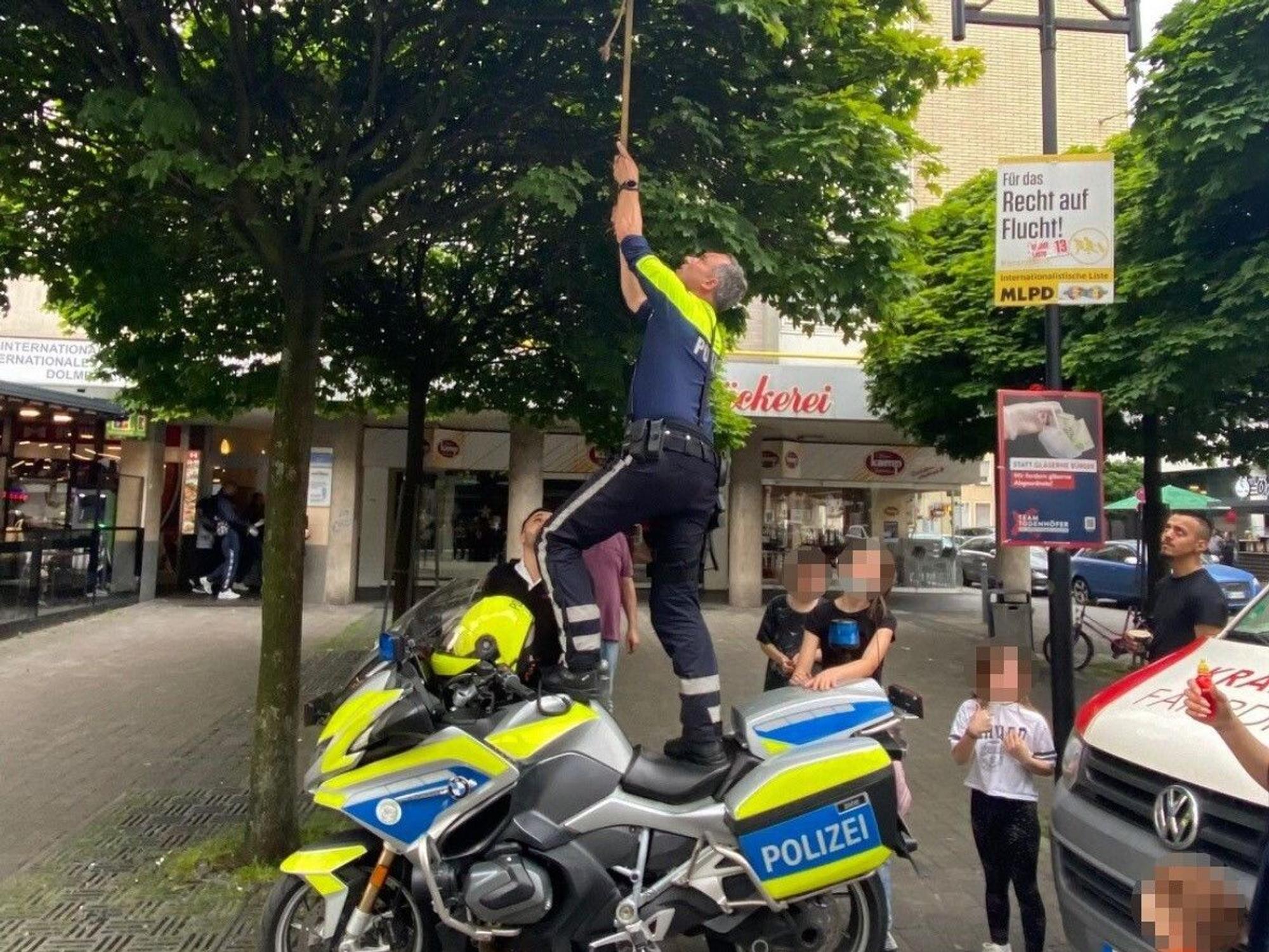 Ein Motorradpolizist aus Hagen steht auf seinem Motorrad, um einen Ball aus einem Baum zu holen.