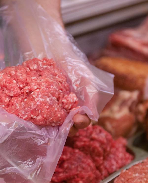 Ein Mitarbeiter eines Fleischerei-Fachgeschäfts hält eine Portion Mett in der Hand.