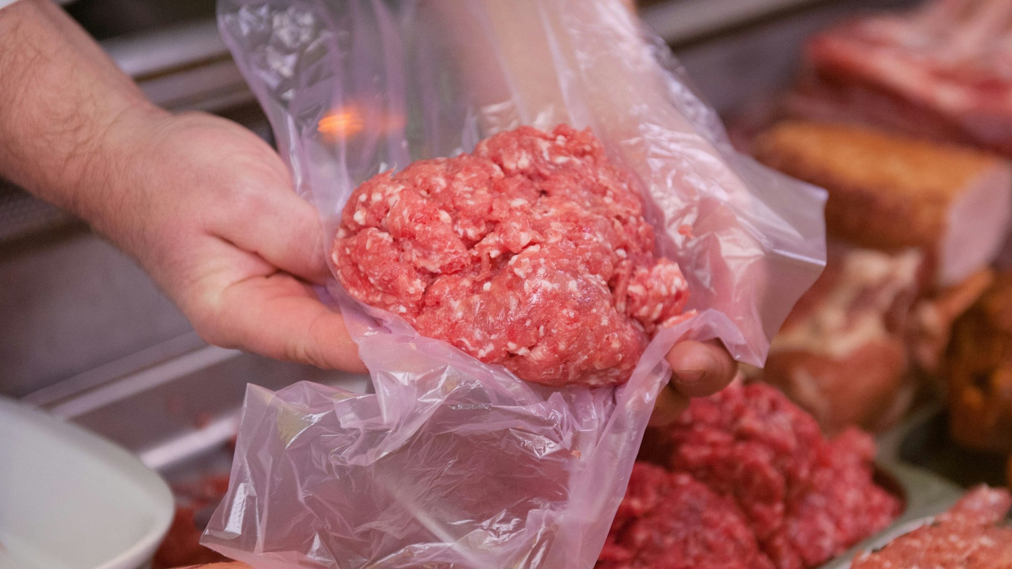 Ein Mitarbeiter eines Fleischerei-Fachgeschäfts hält eine Portion Mett in der Hand.