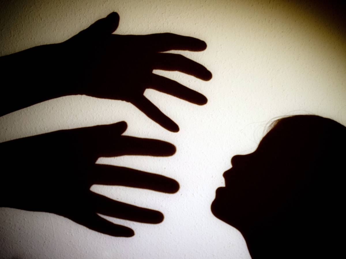 Schatten von Händen einer erwachsenen Person und dem Kopf eines Kindes sind an einer Wand eines Zimmers zu sehen.