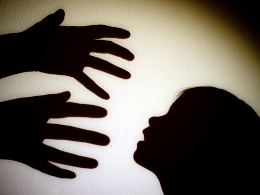 Schatten von Händen einer erwachsenen Person und dem Kopf eines Kindes sind an einer Wand eines Zimmers zu sehen.