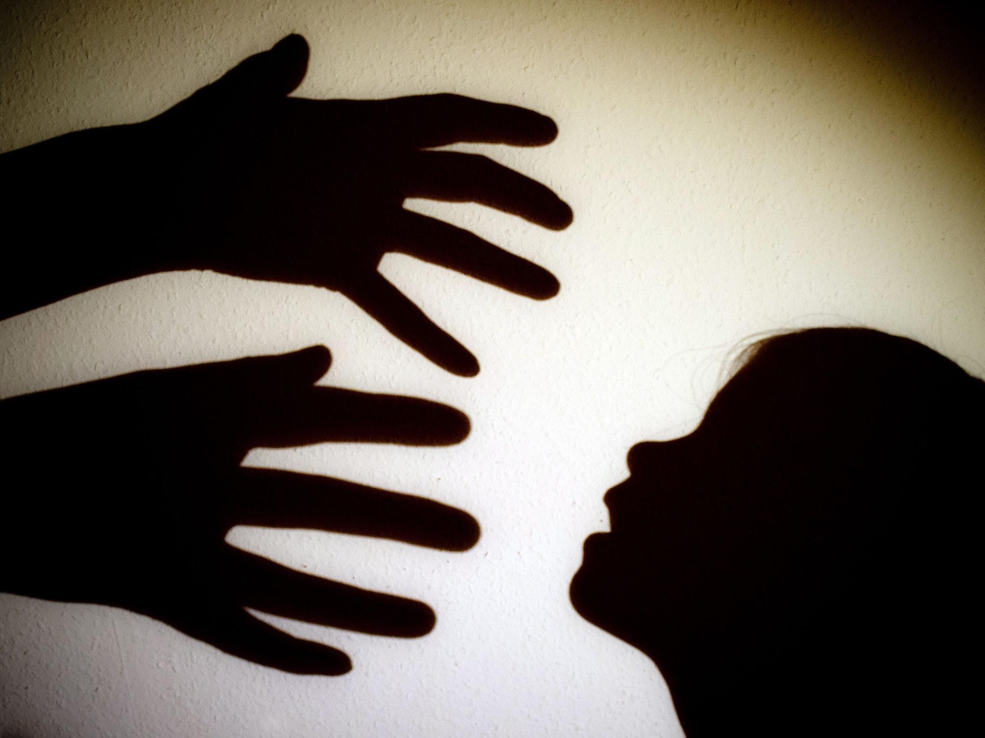 Schatten von Händen einer erwachsenen Person und dem Kopf eines Kindes sind an einer Wand eines Zimmers zu sehen.