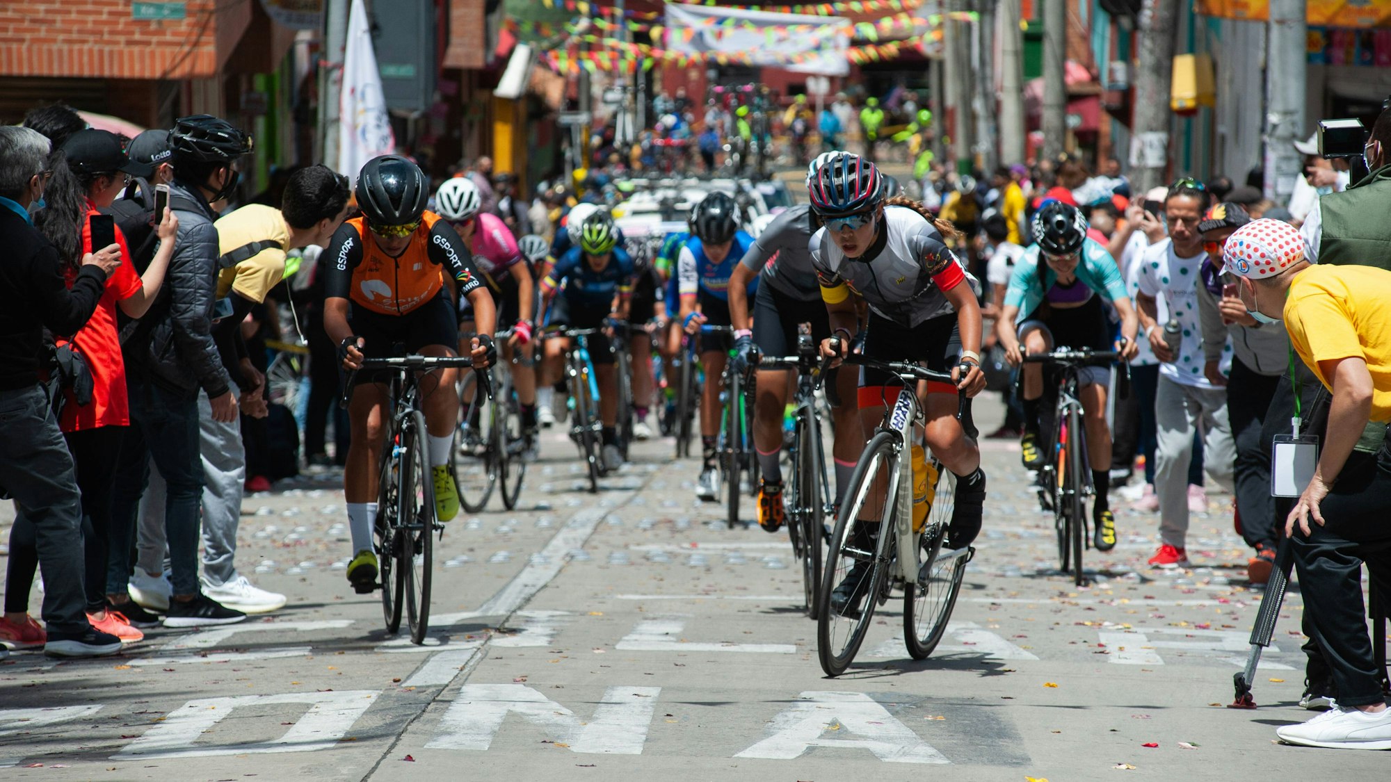 Die Rad-Profis kämpfen sich bei der Vuelta a Colombia auf einer schmalen Gasse den Berg hoch – Fans feuern von allen Seiten an.