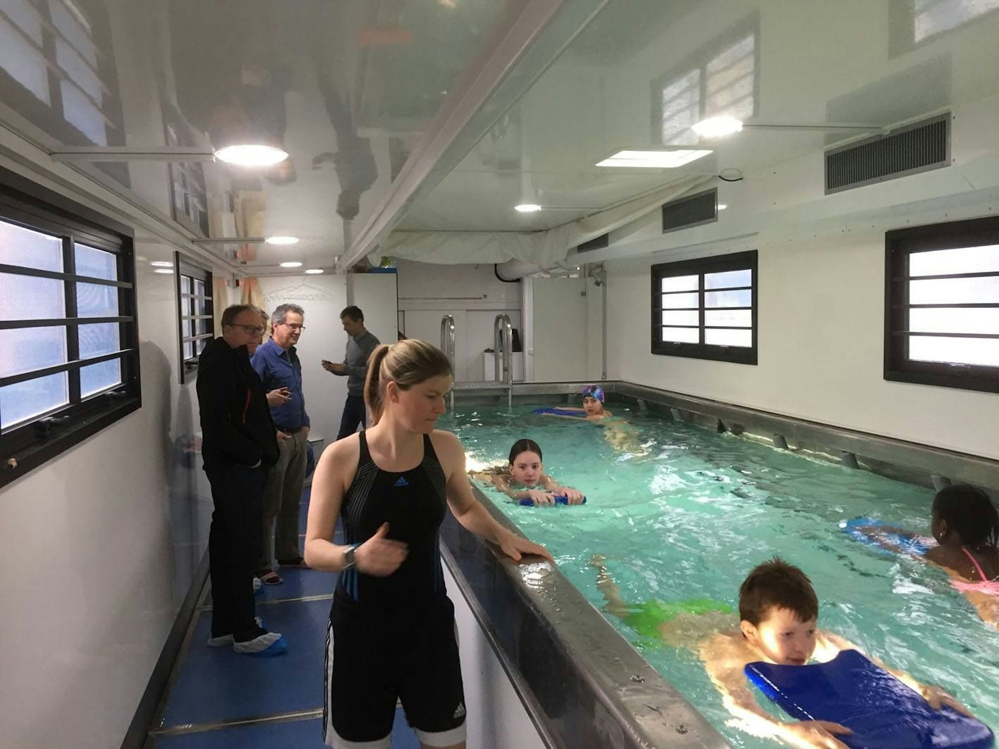 Kinder schwimmen in einem Schwimmbadanhänger. Eine Schwimmlehrerin begleitet die Kinder dabei.