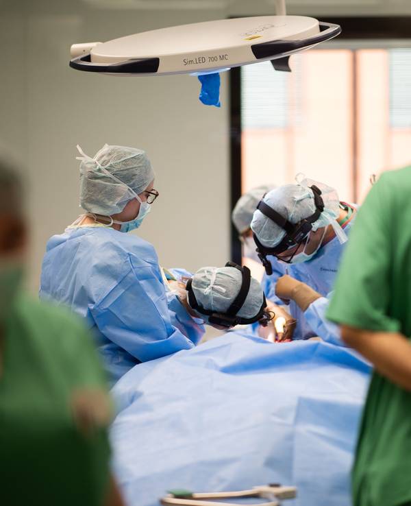 Ein Team aus Ärzten und OP-Helfern steht in einem Operationssaal während einer Operation um einen Patienten.