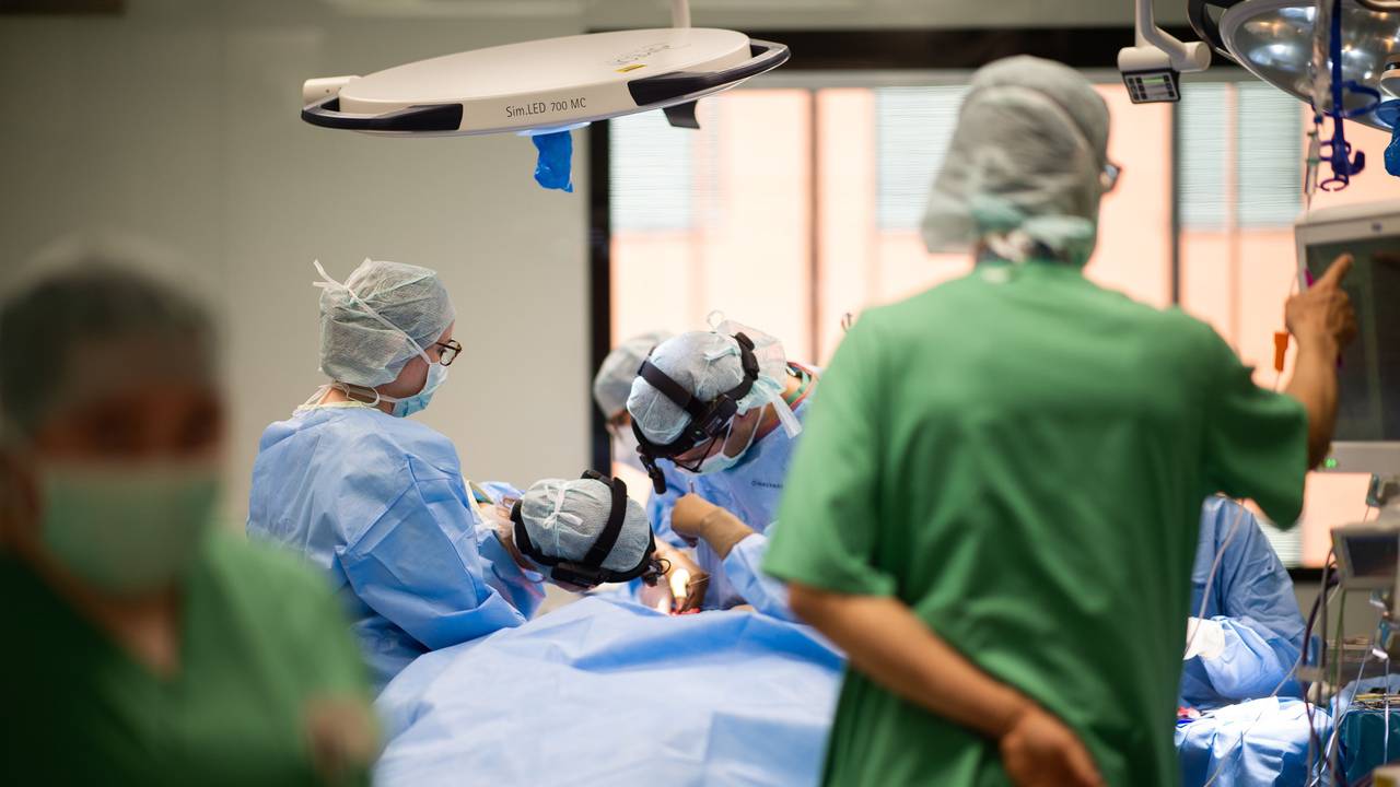 Ein Team aus Ärzten und OP-Helfern steht in einem Operationssaal während einer Operation um einen Patienten.