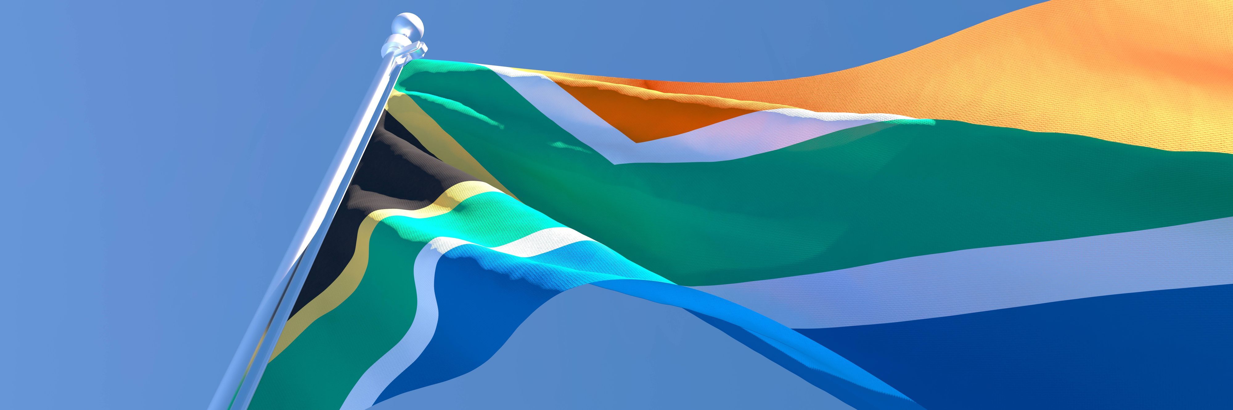 Die südafrikanische Flagge weht im Wind vor blauem Himmel.