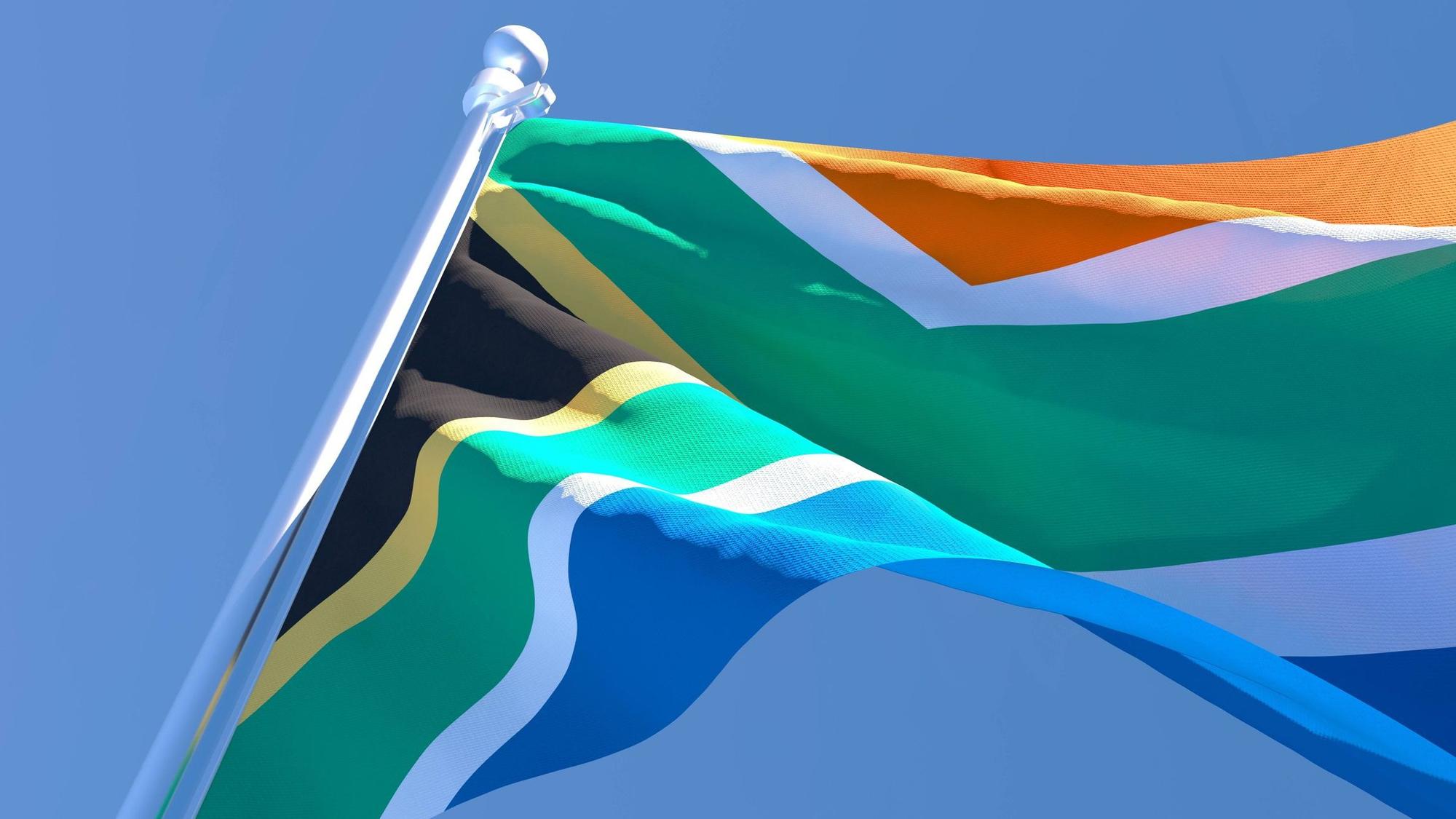 Die südafrikanische Flagge weht im Wind vor blauem Himmel.
